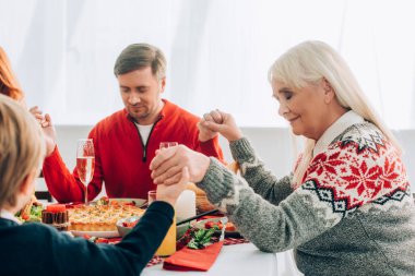 Selective focus of positive grandmother holding hands with family at home clipart