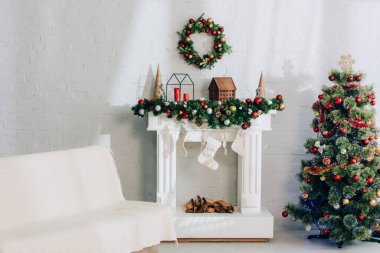 Şöminenin yanında battaniyeli kanepe, Noel çorapları ve süslü çam ağaçları.