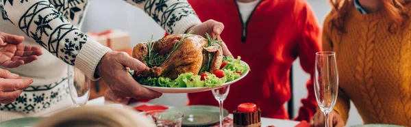 家で家族の近くのお祝いのテーブルの上で七面鳥を提供する男のパノラマショット — ストック写真