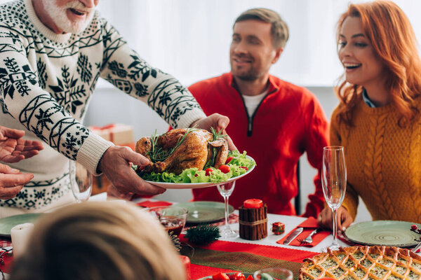 Selective focus of granddad serving turkey on festive table near family at home