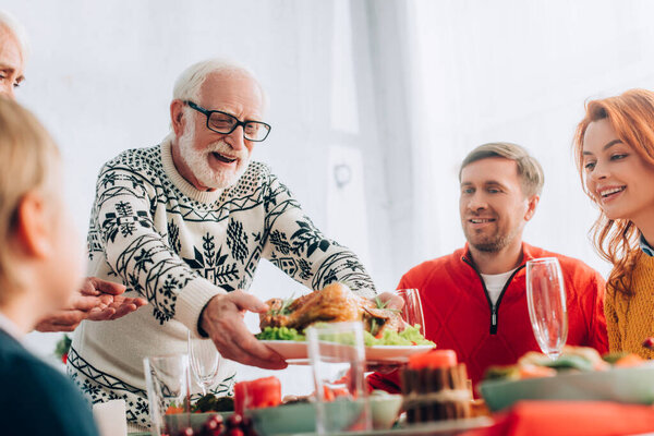 Selective focus of happy grandfather serving turkey on festive table near family