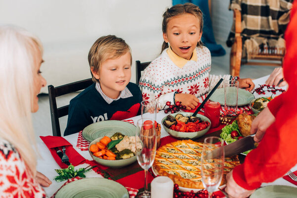 Selective focus of excited children looking at pie on festive table at home