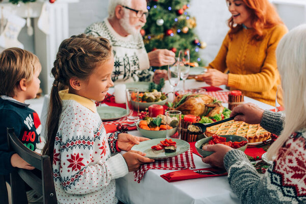 Selective focus of girl with plate near grandmother serving vegetables at home