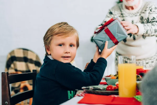 テーブルに座っている祖父からのギフトボックスを保持する小さな男の子の選択的な焦点 — ストック写真