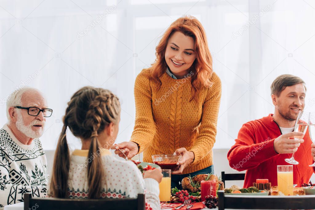 Redhead woman serving sauce on plate near family at festive table