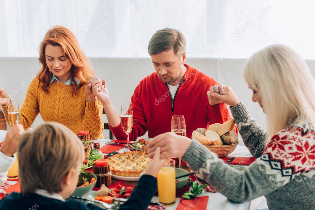 Selective focus of woman and man holding hands with family, sitting at table