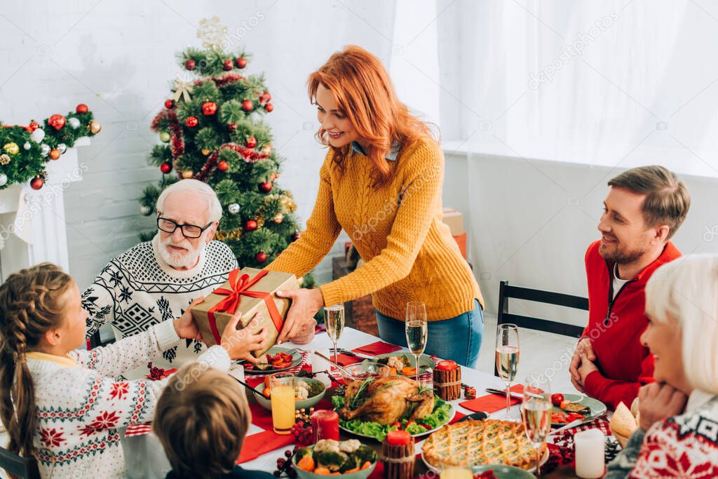 Mother greeting daughter with present, standing near family at festive table