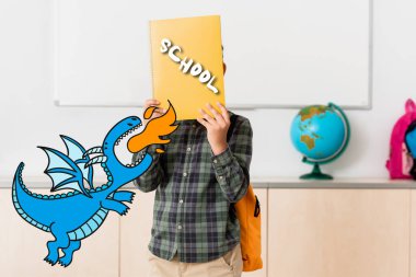 Okuldaki okul çocuğu, elinde yüzün yanında kitap ve dinozor çizimi tutuyor. 