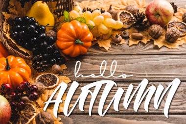 autumnal harvest in basket on foliage near hello autumn lettering on wooden background clipart