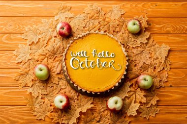 Şükran Günü balkabağı turtasının en üst görüntüsü. Yaprakların yanında elmalar var. Ahşap arka planda Ekim harfleri.