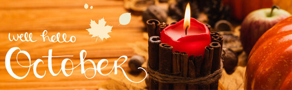 selective focus of burning candle with autumnal decoration near well hello october lettering on wooden background, panoramic shot