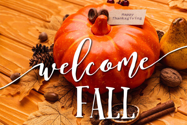 pumpkin with autumnal decoration and happy thanksgiving card near welcome fall lettering on wooden background