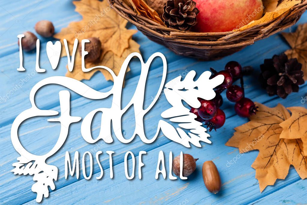 autumnal leaves, berries, acorns and cones near i love fall most of all lettering on blue wooden background