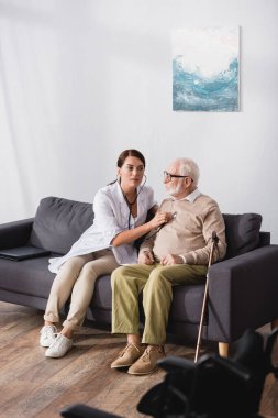 geriatric nurse checking heath of aged man with stethoscope clipart