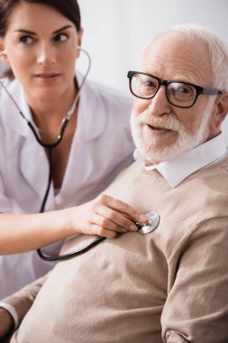 Tıbbi asistan, geçmişi bulanık steteskoplu yaşlı adamı muayene ediyor.