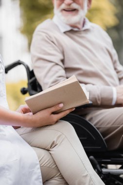Yaşlı hemşirenin dışarıda bulanık arka planda engelli bir adama kitap okuması.