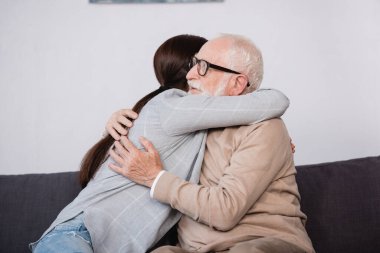 Yaşlı baba ve yetişkin kızın evde kucaklaşması.