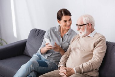 Neşeli kadın cep telefonunu işaret ediyor. Neredeyse kafası karışmış yaşlı baba.
