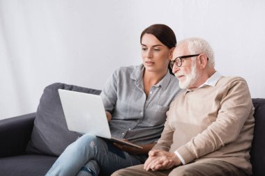 Yetişkin esmer kadın, yaşlı babasıyla birlikte dizüstü bilgisayar kullanıyor.