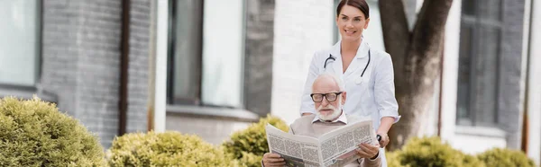 Веселая Пожилая Медсестра Гуляет Инвалидом Пожилой Человек Читает Газету Баннер — стоковое фото