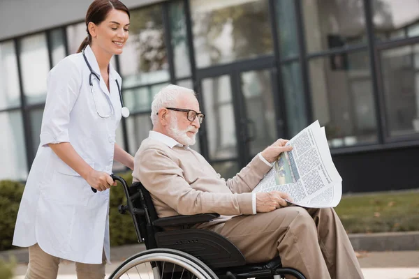 Handicapped Aged Man Reading Book Wheelchair While Walking Geriatric Nurse — Stock Photo, Image