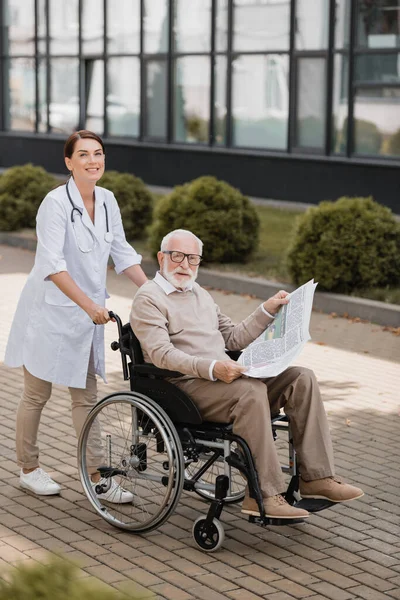 Allegro Assistente Sociale Guardando Fotocamera Mentre Cammina Con Uomo Handicappato — Foto Stock