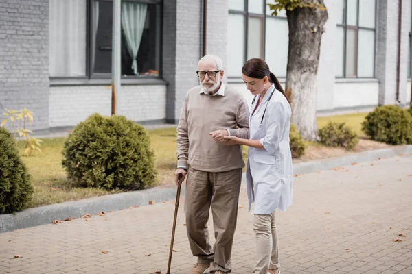 Social Worker Supporting Man Walking Stick While Strolling Together — Stock Photo, Image