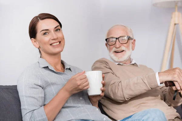 Happy Woman Cup Tea Looking Camera While Sitting Cheerful Father — Stock Photo, Image