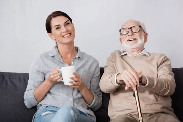 Cheerful Woman Laughing Elderly Father Looking Camera While Sitting Sofa — Stock Photo, Image