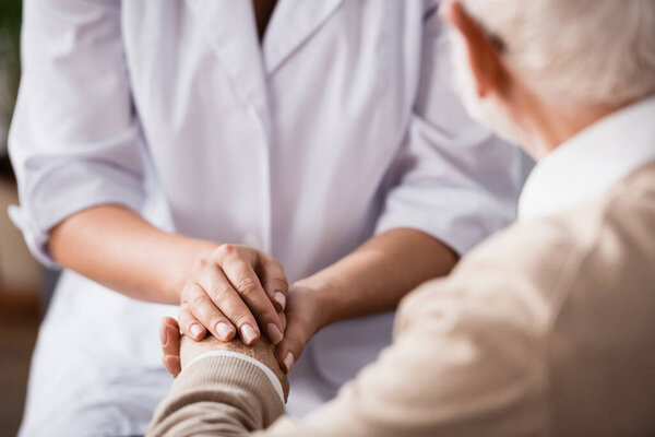 cropped view of social worker holding hands of aged man on blurred background