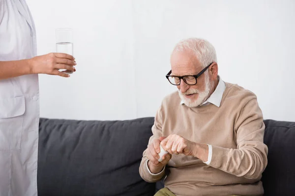 Ηλικιωμένος Άνδρας Κρατώντας Χάπια Ενώ Ιατρική Βοηθός Ποτήρι Νερό — Φωτογραφία Αρχείου
