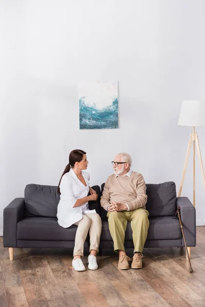 Aged Man Eyeglasses Talking Geriatric Nurse While Sitting Sofa Home — Stock Photo, Image
