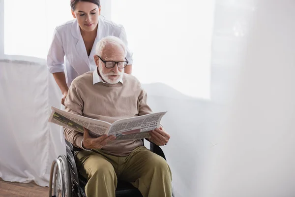 Asistentă Medicală Geriatrică Lângă Bătrân Handicapat Care Citește Ziare Scaun — Fotografie, imagine de stoc