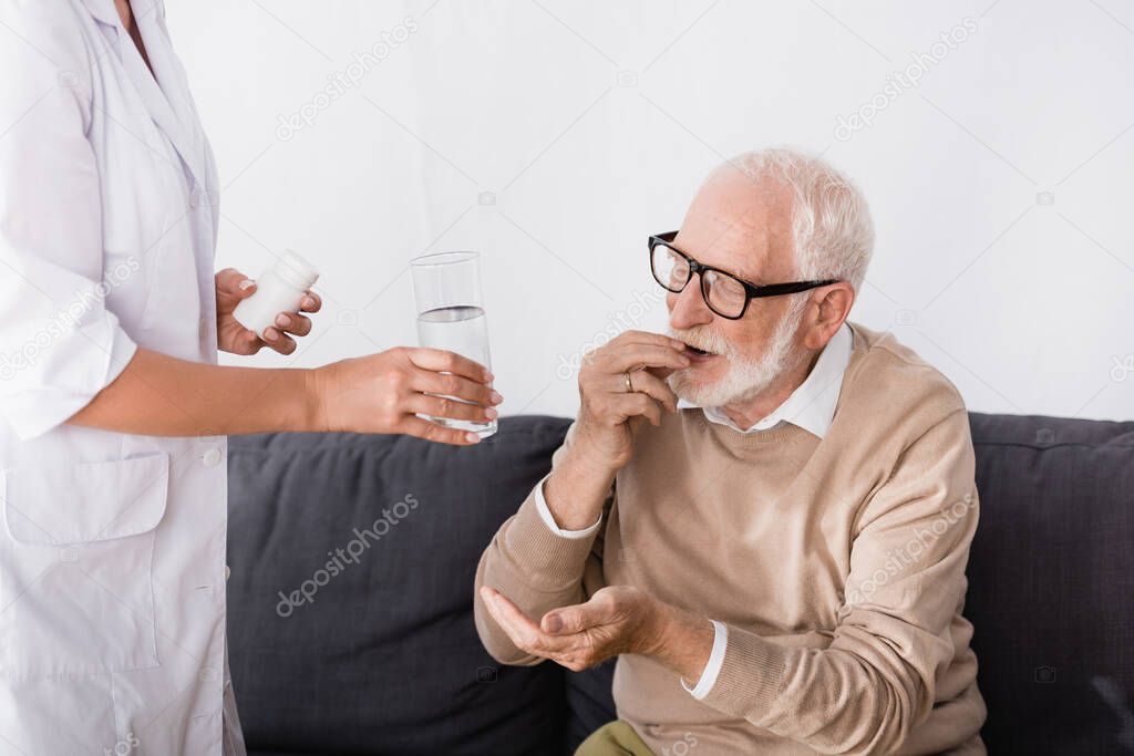 nurse holding pills and water near aged man