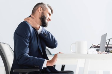 Resmi olarak iş adamı laptopun yanında boynu ağrıyan birini giyer ve ofisteki bulanık önplanda fincan takar. 