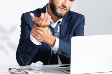 Kırpılmış iş adamı görüşü. Aletlerin yanında kol ağrısı ve masa üstünde yığılmış kağıt. 