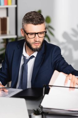 Bulanık önplan üzerinde çalışırken elinde kağıtlar tutan bir işadamı 