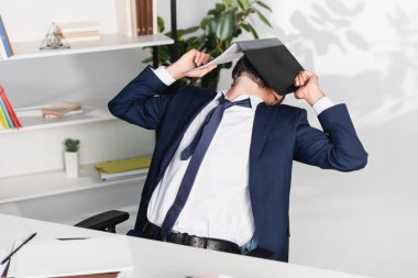 Ofisteki bulanık ön planda masanın yanında kağıt klasörüyle yüzünü kaplayan işadamı 