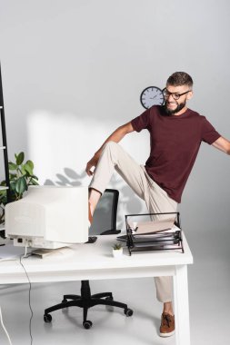 Angry businessman kicking computer monitor near stationery in office  clipart