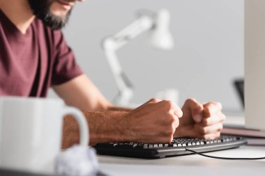 Stresli iş adamının bilgisayar klavyesini bardakla ve bulanık ön planda birikmiş kağıtla dövdüğü görüntüler 