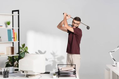 Sinirli işadamı bilgisayarın yanında golf sopası ve ofis masasında belgeler tutuyor. 