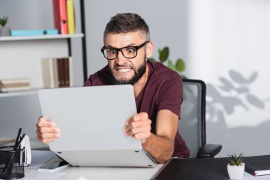 Ofisteki bulanık ön planda kağıt klasörünün yanında dizüstü bilgisayar tutan çılgın işadamı 