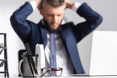 Yorgun işadamının yanındaki ofis masasında gözlük ve kırtasiye malzemeleri. 