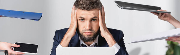 Tired businessman looking at camera near colleagues holding smartphone and paper folders in office, banner