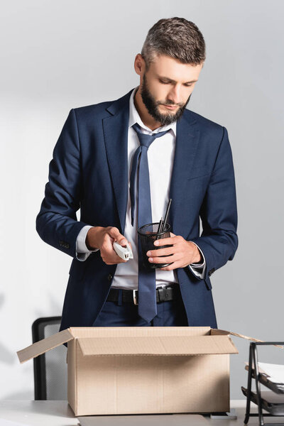 Fired businessman holding stationery near cardboard box in office 