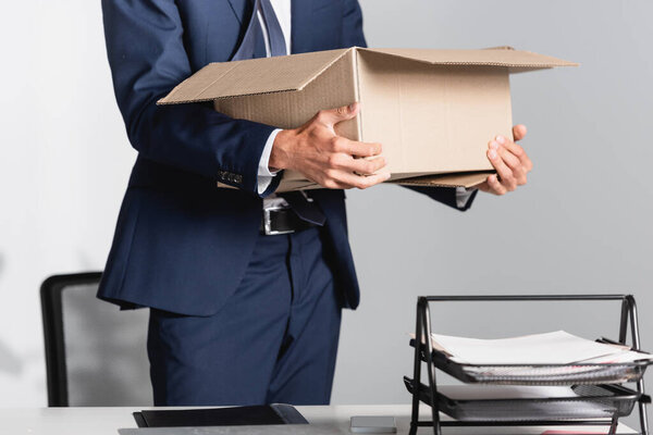 Cropped view of fired businessman holding carton box near papers on blurred foreground 