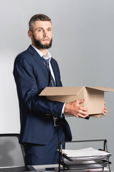 Dismissed businessman with carton box looking at camera near smartphone and papers on table 