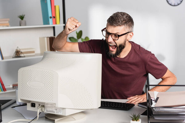 Screaming businessman with hand in fist looking at computer on office table 