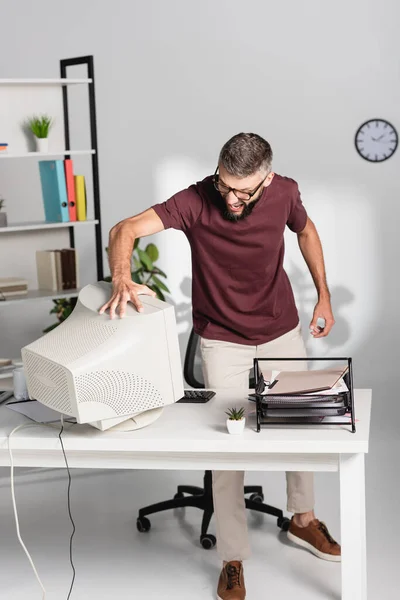 一个咄咄逼人的商人一边在办公室桌上的文件旁边摸着电脑显示器一边尖叫 — 图库照片