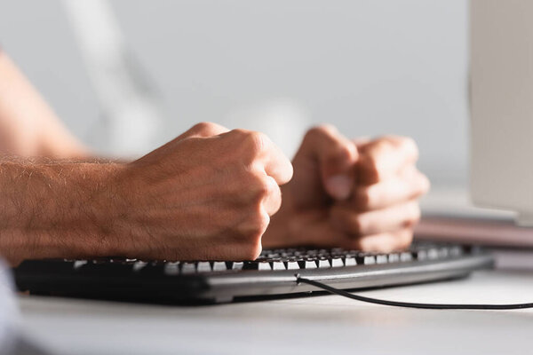 Cropped view of businessman beating computer keyboard in office 